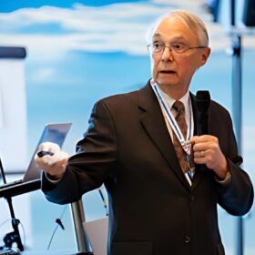 A well-dressed man in a suit and tie speaks confidently at a podium during a formal event.