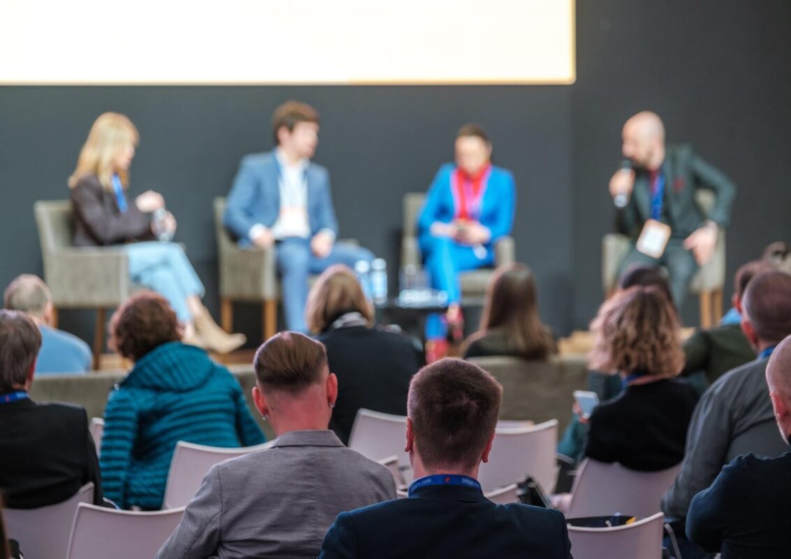A diverse group of people seated in chairs, engaged in discussion at a conference setting.