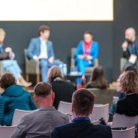 A diverse group of people seated in chairs, engaged in discussion at a conference setting.